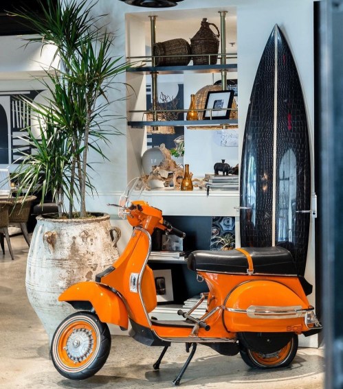 An orange scooter parked beside a surfboard and decorative shelves in a stylish interior space.