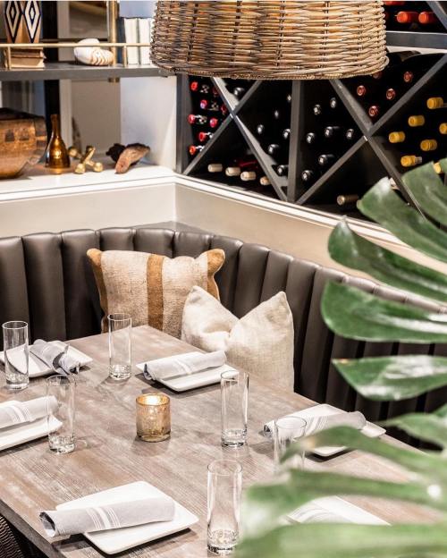 Cozy restaurant table setting with a wooden table, elegant glassware, and a wine display in the background.