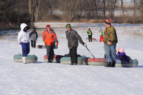 A group of people in winter clothing enjoying tubing on a snowy hill, with some waiting and others preparing to slide.