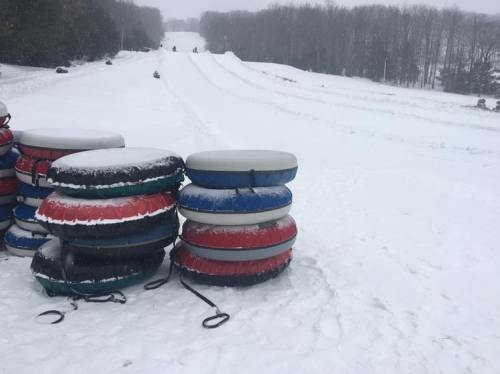 A stack of colorful snow tubes on a snowy hill, with people sledding in the background.