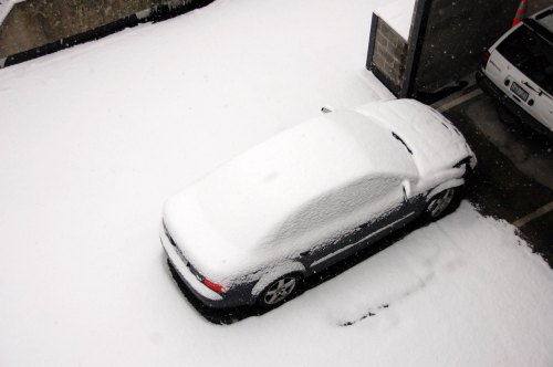 A car covered in a thick layer of snow, parked in a snowy outdoor area.