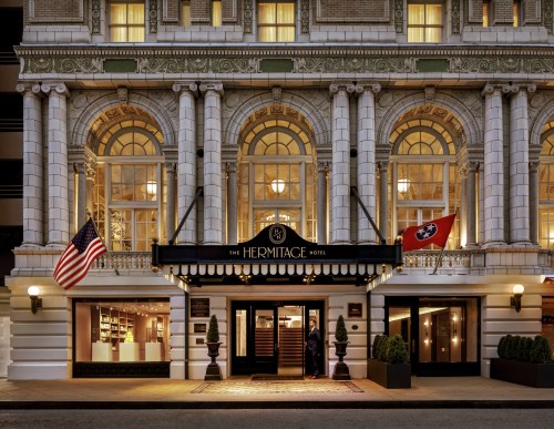 The Hermitage Hotel entrance, featuring elegant architecture, large windows, and American and Tennessee flags.