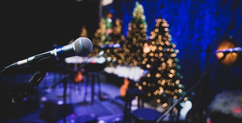 A microphone in focus with blurred Christmas trees and stage instruments in the background, creating a festive atmosphere.