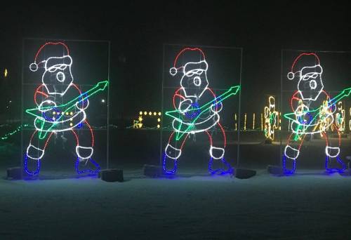 Three illuminated figures of Santa Claus playing electric guitars, decorated with colorful lights against a dark background.