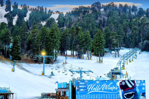 Ski resort scene with snow-covered slopes, chairlifts, and a "Hello Winter" banner amidst tall pine trees.