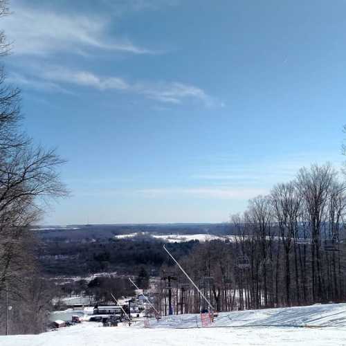 A snowy landscape with ski lifts, trees, and a clear blue sky in the background.