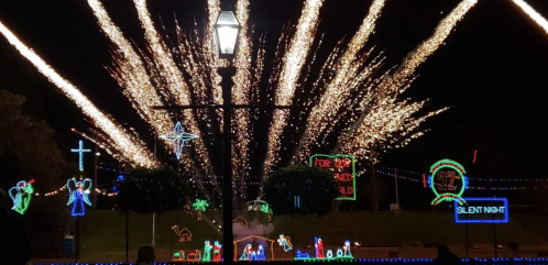 Colorful holiday lights and fireworks illuminate a festive scene with decorations, including angels and a cross.