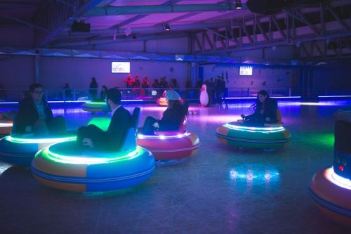 People sitting in colorful bumper cars with neon lights in a lively indoor amusement setting.