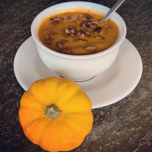 A bowl of pumpkin soup topped with nuts, next to a small orange pumpkin on a dark surface.
