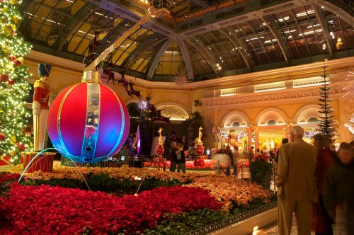 A festive indoor display featuring a large ornament, Christmas trees, and vibrant poinsettias in a holiday setting.