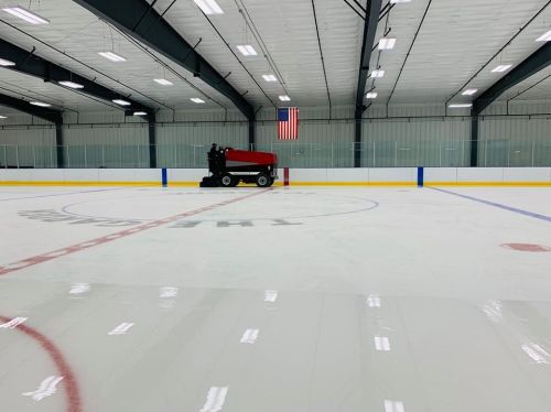 A red ice resurfacing machine on a freshly groomed hockey rink, with an American flag in the background.