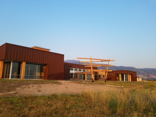 Modern buildings with wooden accents set against a clear sky and mountains in the background, surrounded by grass.