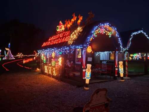 A festive cabin adorned with colorful Christmas lights and decorations, including Santa and holiday figures, at night.