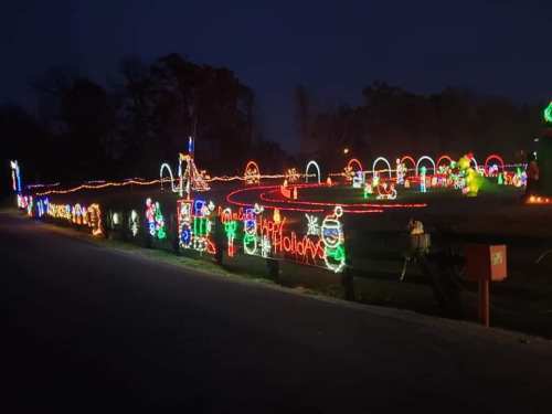 Colorful holiday lights decorate a pathway, featuring festive figures and cheerful messages in a nighttime setting.