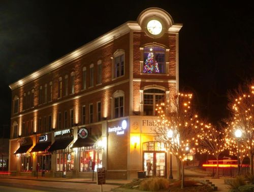 A brick building at night, featuring a clock, holiday decorations, and illuminated trees outside.