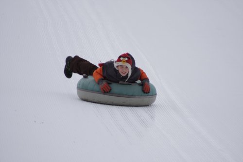 A child in winter clothing joyfully sledding down a snowy hill on a green inflatable tube.