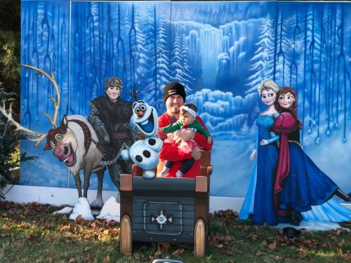 A person and a child pose in front of a winter-themed backdrop featuring characters from "Frozen."