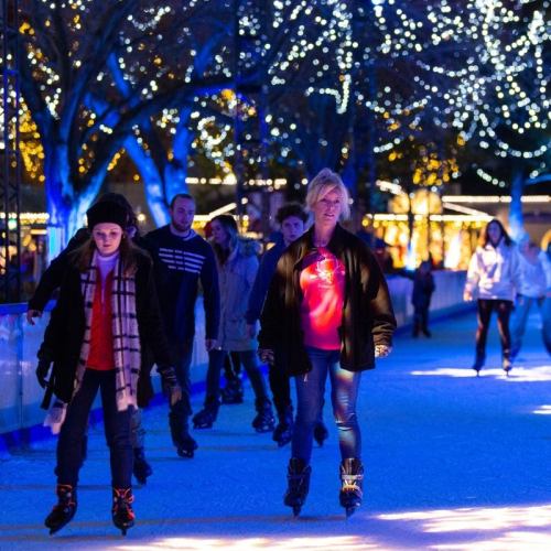 A group of people ice skating at night, surrounded by twinkling lights and festive decorations.