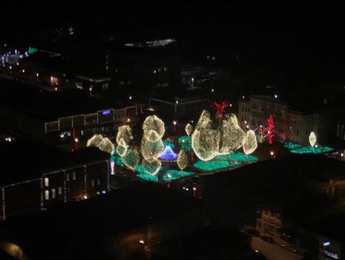 Aerial view of a park illuminated with colorful holiday lights at night, featuring glowing trees and decorative shapes.