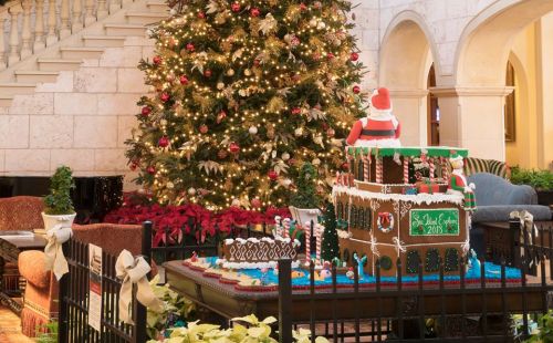 A festive lobby scene featuring a decorated Christmas tree and a large gingerbread house with holiday decorations.