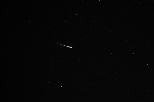 A bright meteor streaks across a dark night sky filled with stars.