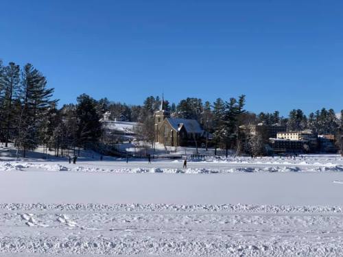 A snowy landscape with a church and trees in the background under a clear blue sky.
