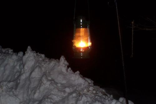 A glowing lantern hangs above a large snowbank at night, illuminating the surrounding darkness.