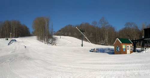 A snowy ski slope with a ski lift, a small lodge, and clear blue skies in the background.