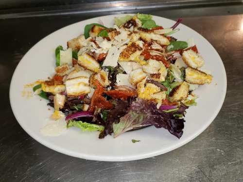 A colorful salad with mixed greens, croutons, cheese, and a sprinkle of seasoning on a white plate.