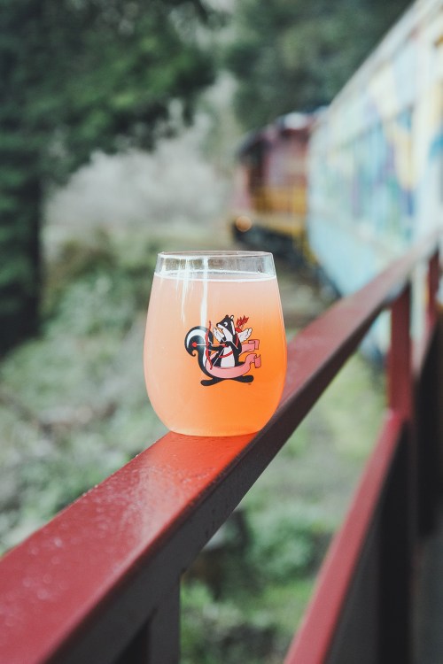 A colorful drink in a glass with a playful design, resting on a red railing with a blurred train in the background.