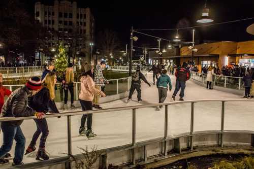 A lively outdoor ice skating rink at night, filled with skaters and festive lights, surrounded by a crowd.