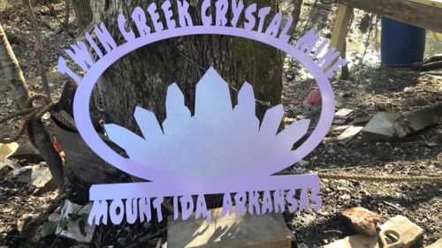 Sign for Twin Creek Crystal Mine in Mount Ida, Arkansas, featuring a crystal design and surrounded by natural scenery.
