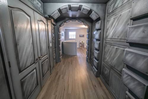 A hallway with textured gray walls and doors, leading to a bright room with wooden flooring and furniture in the background.