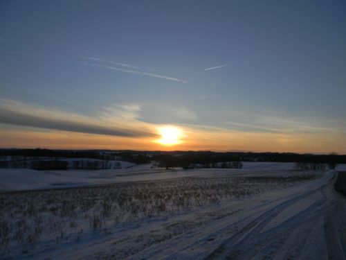 A serene winter landscape at sunset, with snow-covered fields and a colorful sky.