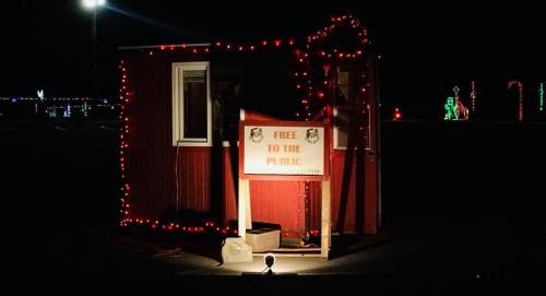 A small red booth decorated with lights, featuring a sign that reads "Free to the Public," set against a dark night.