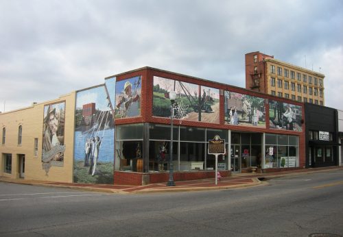 A colorful mural decorates a building corner, depicting local scenes and history, with a cloudy sky above.