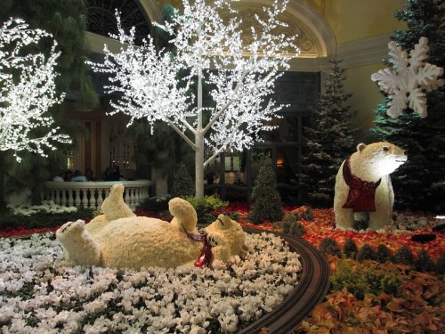 A festive display featuring polar bears among white flowers and illuminated trees, creating a winter wonderland scene.