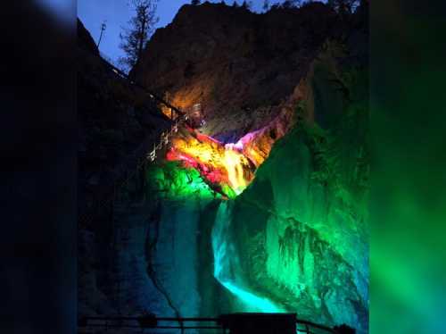 A colorful waterfall illuminated at night, cascading down rocky cliffs with vibrant lights.