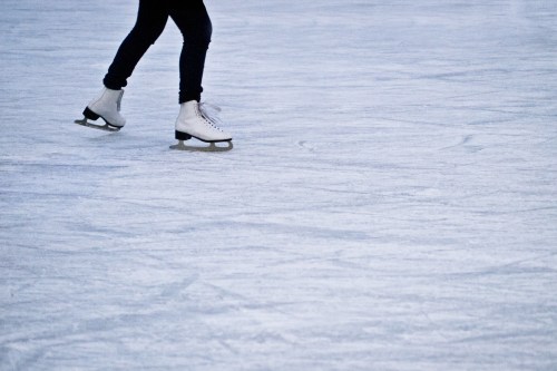 A person skating on ice, wearing white skates and dark pants, gliding across a smooth, icy surface.