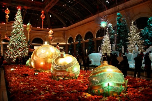 A festive display featuring large ornaments, Christmas trees, and colorful lights in a beautifully decorated indoor space.