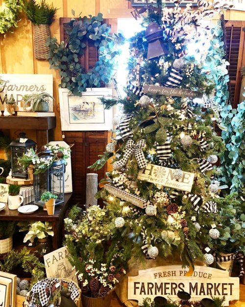 A decorated Christmas tree surrounded by greenery and rustic signs, featuring a farmers market theme.