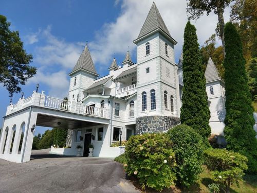 A large, ornate white mansion with pointed towers and a stone facade, surrounded by greenery and under a blue sky.