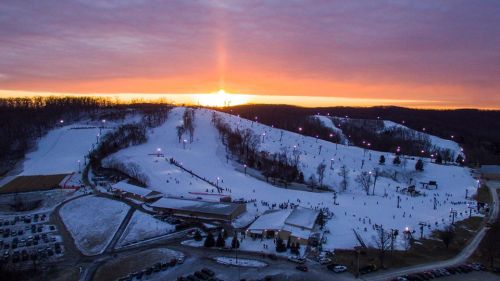 A snowy ski resort at sunset, with skiers on the slopes and a colorful sky in the background.