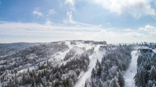 A snowy landscape with mist rising over trees and hills under a bright blue sky.