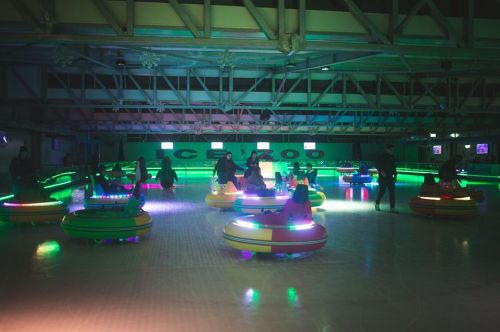 A vibrant indoor ice rink with colorful bumper cars and people enjoying the ride under neon lights.