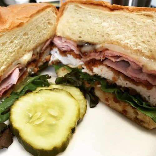 Close-up of a sandwich with layers of meat, cheese, lettuce, and a pickle slice on the side.