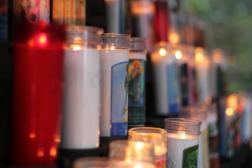 A close-up of lit candles in various colors and designs, creating a warm, glowing atmosphere.