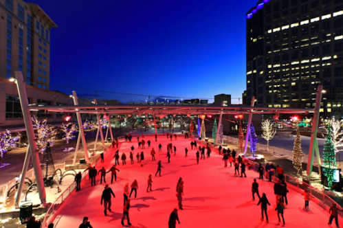 A vibrant ice skating rink at night, illuminated by colorful lights and surrounded by festive trees.