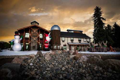 A festive scene featuring a large house with holiday decorations, including inflatable snowmen, Santa, and reindeer.