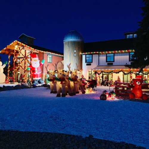 A festive outdoor scene with a large Santa, reindeer decorations, and colorful lights on a snowy night.